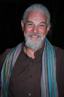 [portrait of smiling man with silvery hair, beard, and moustache, wearing a maroon shirt with turquoise striped fabric scarf]