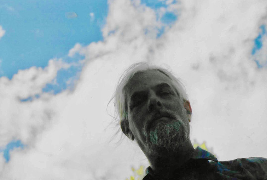 [posterized image of man with moustache and beard looking down to camera with background of white clouds and blue sky]
