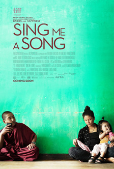 [poster of seated young monk holding cell phone near sead woman and child against a light green painted wall under brown Sing Me A Song text]