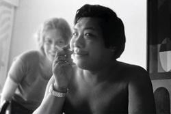 [bare chested man with cigarette, with blonde woman smiling at his side]
