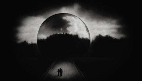 [black and white image of large view of earth against white clouds and black sky, with a highlighted small silhouette of a couple in a dark foreground]