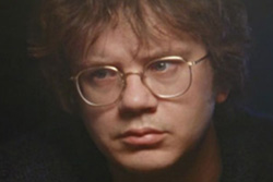 [close up of young man with brown bangs and large round wire-framed glasses looks depressed]