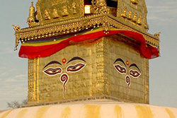 [gold covered stupa with painted face on each side of top, draped with red and gold banner]