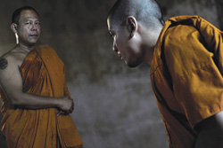 [wearing gold colored robes, a younger Thai monk bows to a senior monk]