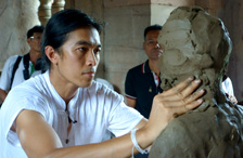 [An Asian man works clay in a sculpture of a life-sized figure.]