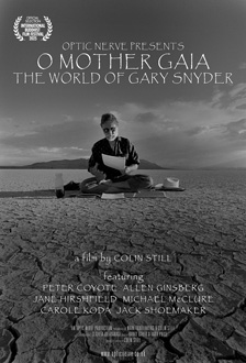 [film poster with grayscale image of a bearded man with sunglasses sitting cross legged on a thin mat on dry cracked earth with a small mountain range in the distance, with white hat to his left and bottle and black cup to his right, looking down at a white paper in his left hand, and stacked white text optic nerve presents o mother gaia the world of gary snyder above the figure and additional lines of white text stacked below the figure, and white laurels on either side of stacked white text official selection international buddhist film festival series, in the upper left corner]