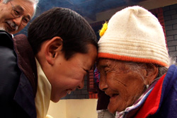 [young Tibetan boy and old Tibetan woman smile and press foreheads in greeting]