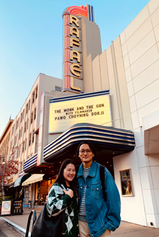 [asian couple standing in front of rafael theater marquee that says the monk and the gun with filmmaker pawo choyning dorji]